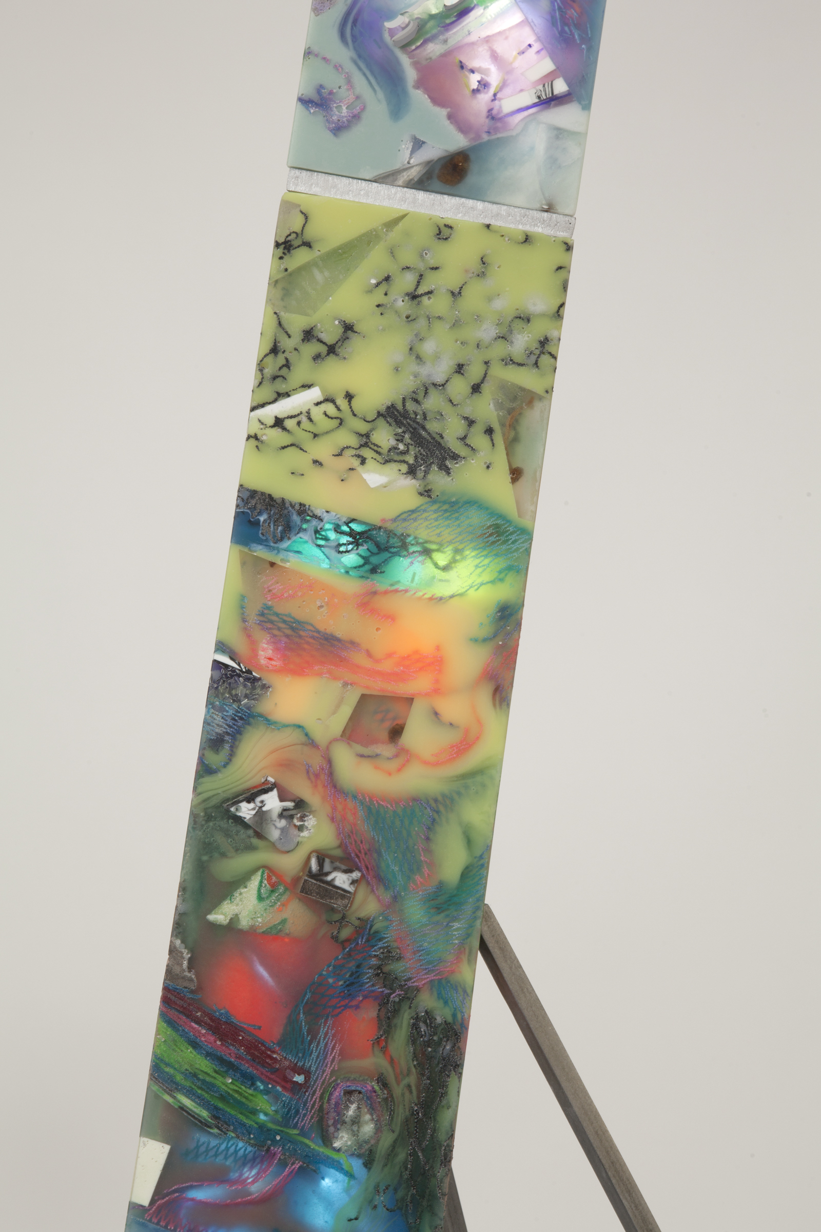 close up of resin pillar with a variety of material inlays and colors. Mostly green and light blue with some orange and black details.