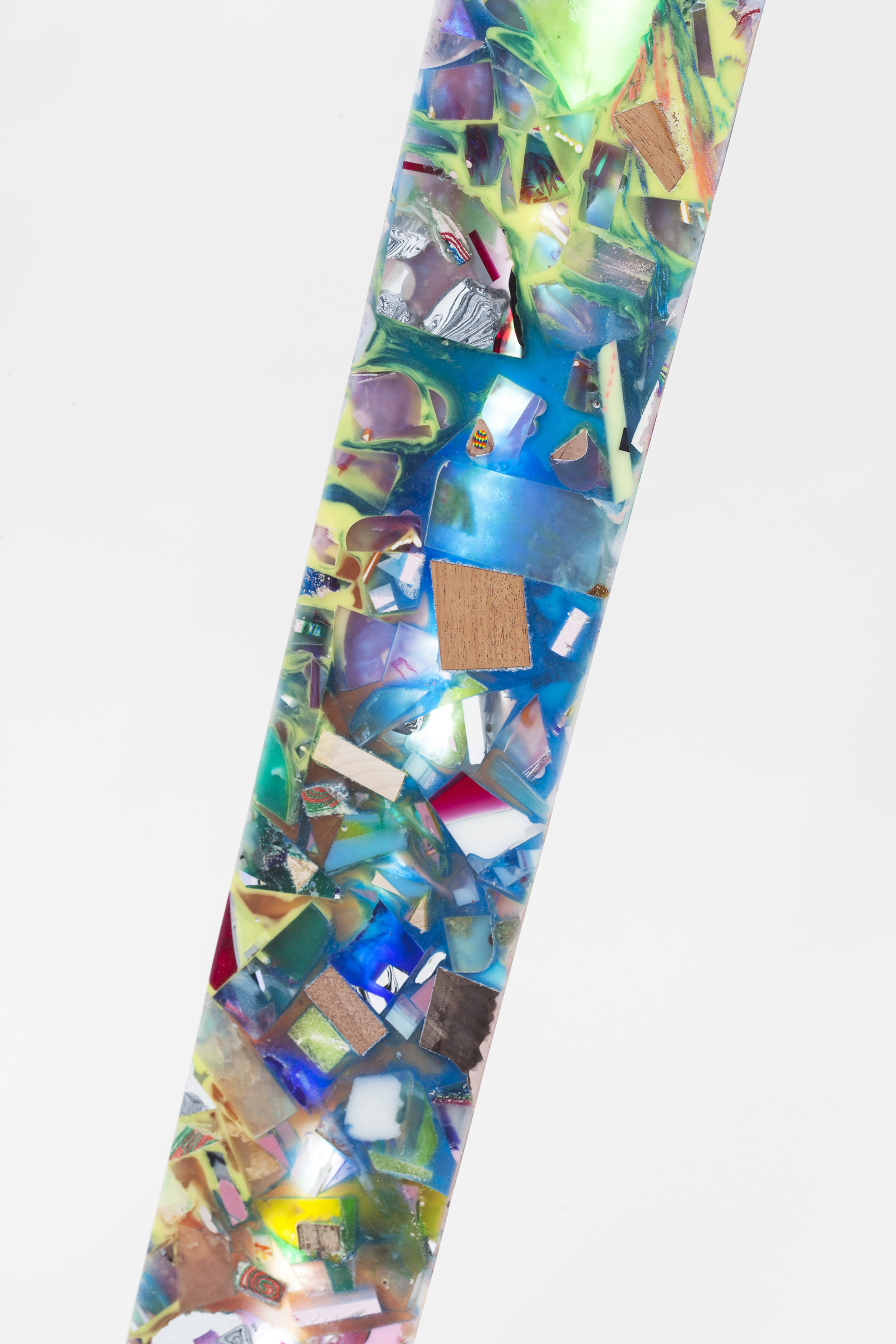 close up of resin pillar with a variety of material inlays and colors, mostly blue and green with specks of tan, red, white, yellow, and more.