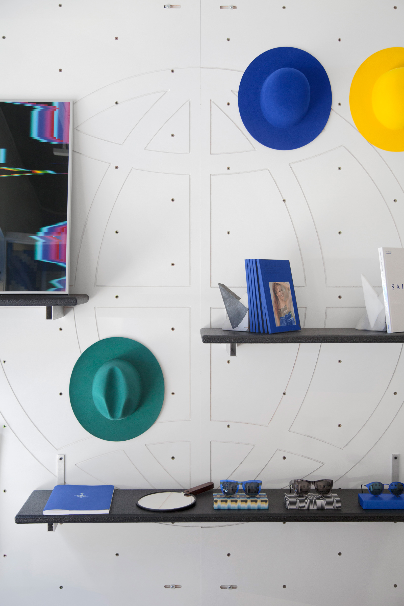 white preforated wall with colorful hats and black shelving.