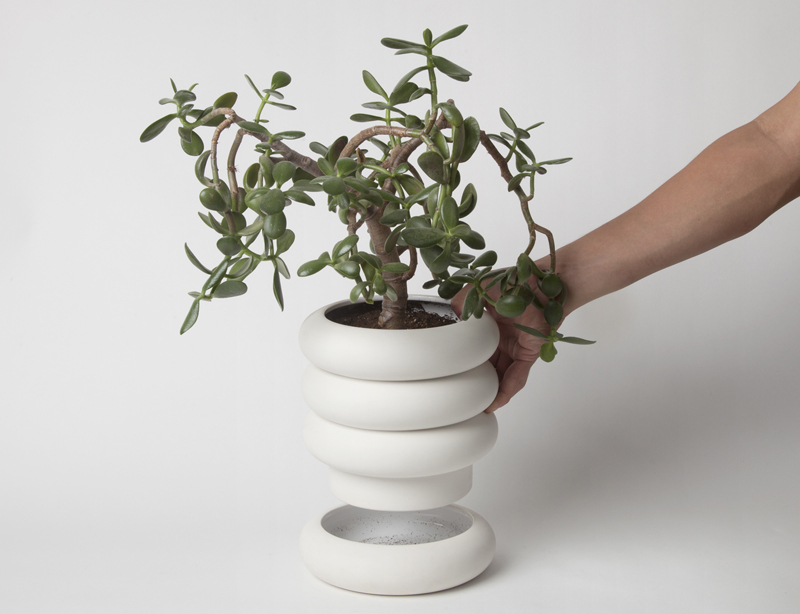 four tier stacking planter with plant inside, being lifted by hand to show water dish.