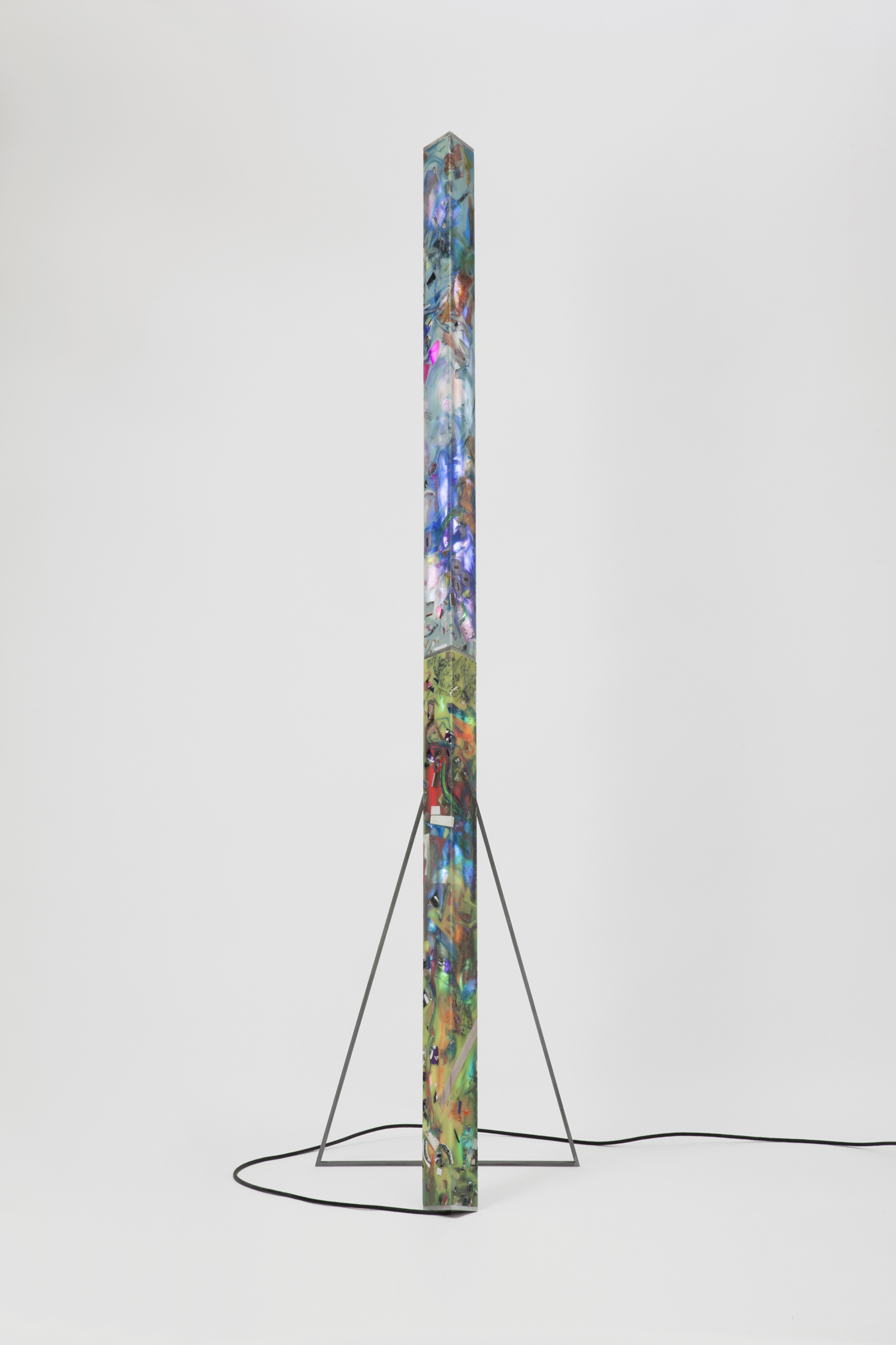 floor lamp consisting of a long pillar of resin of various colors and material inlays, triangular black metal frame and cord.