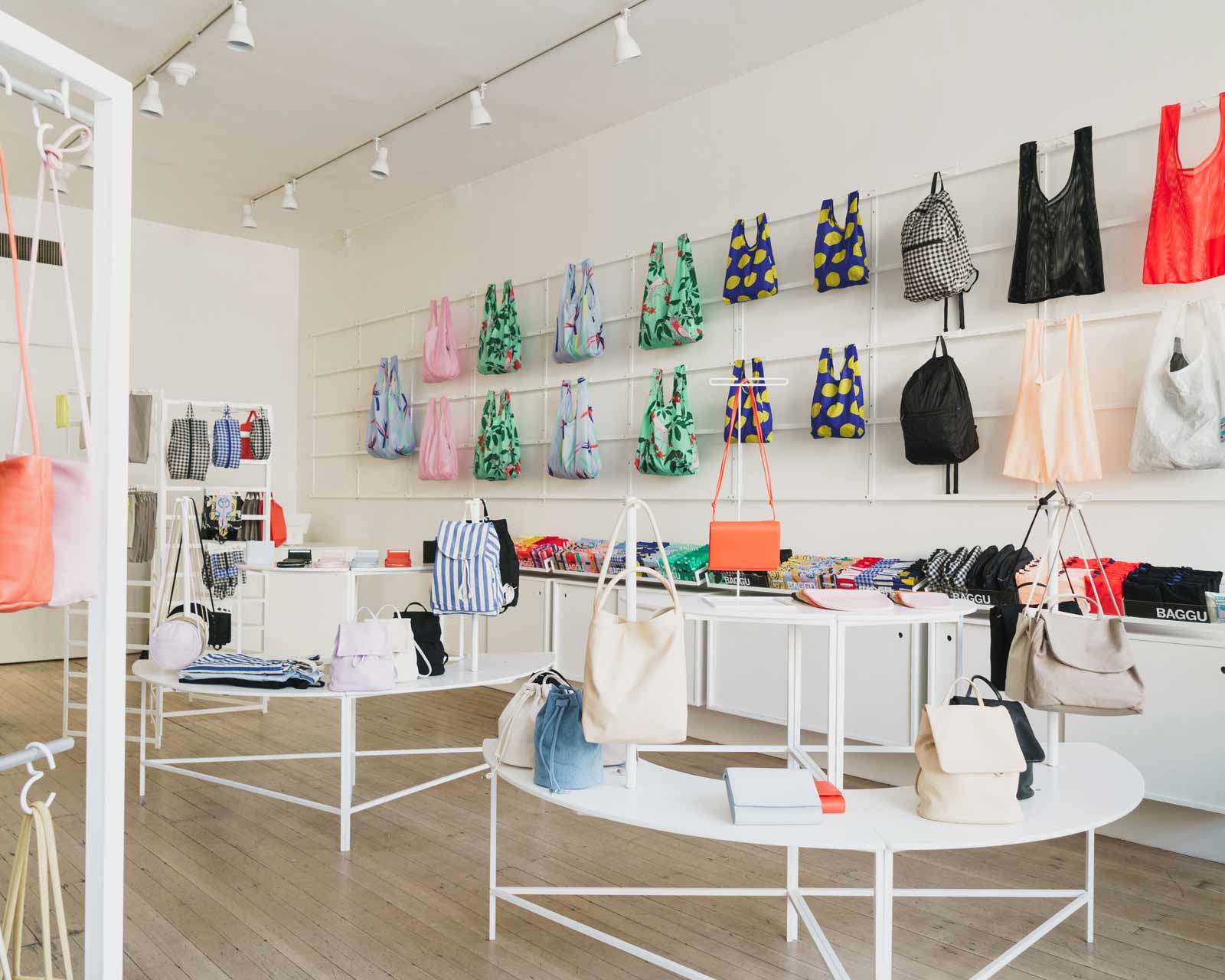 BAGGU storefront with white tiered shelving systems and bag hanging wall systems.