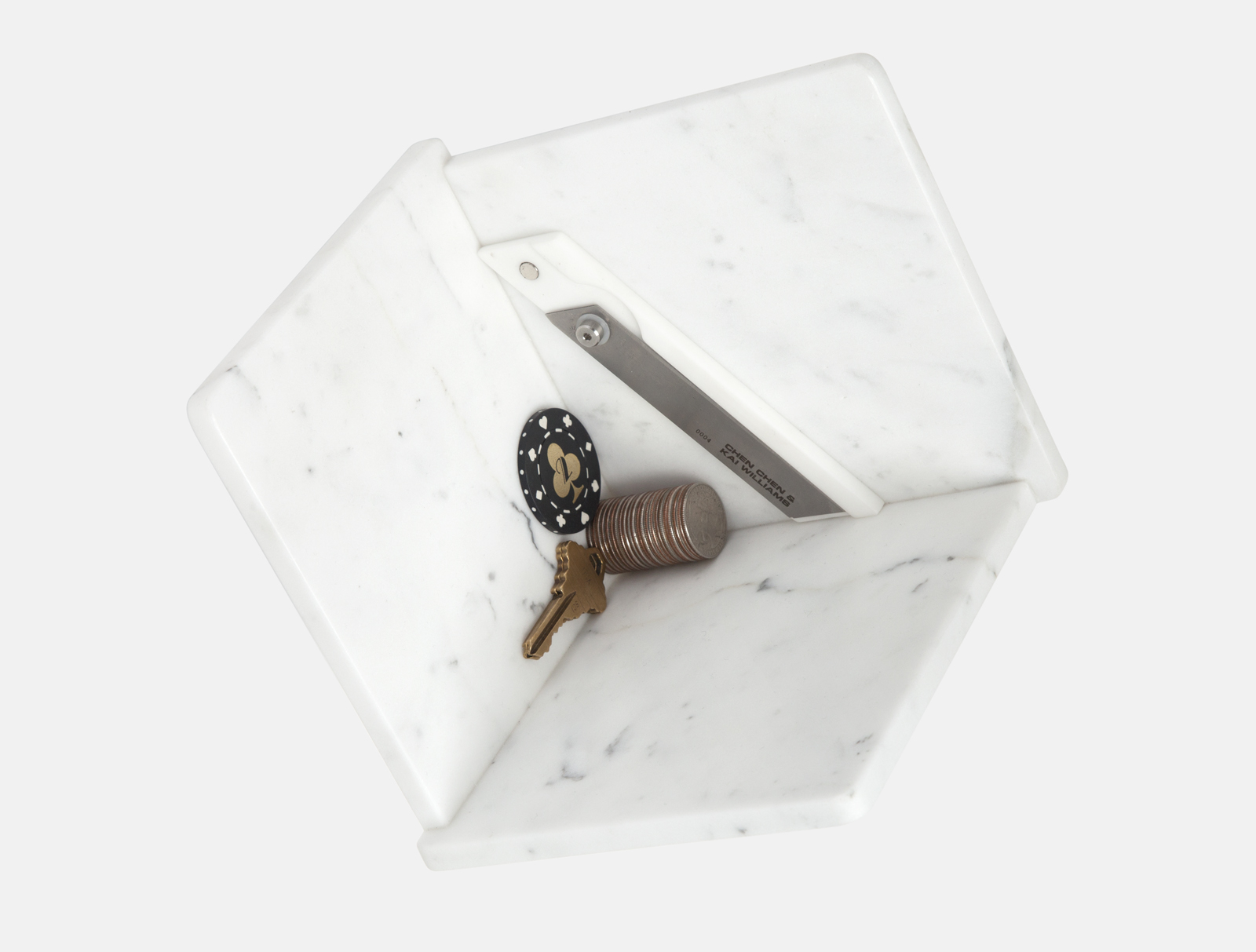 a utility knife, a key, a poker chip and coins in a three sided marble box