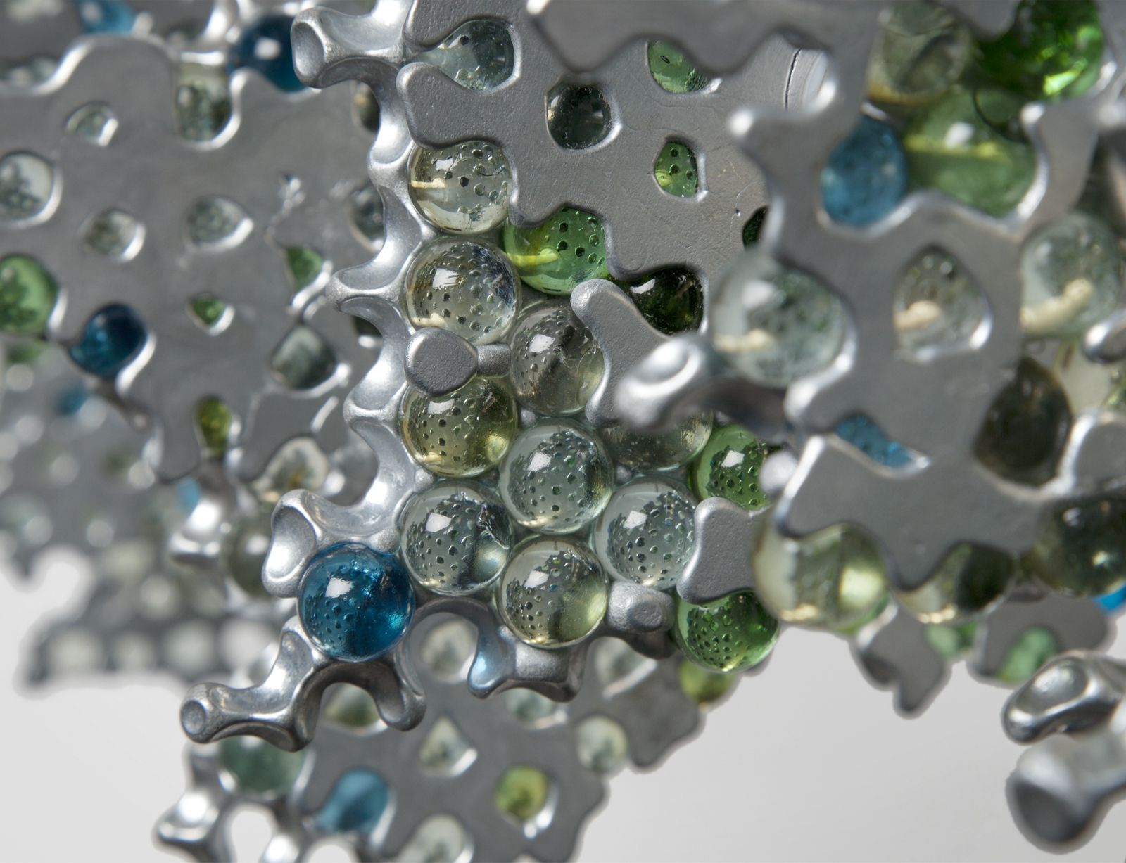 close up of clear, blue, and green glass marbles held together melted aluminum panels on LED strip.