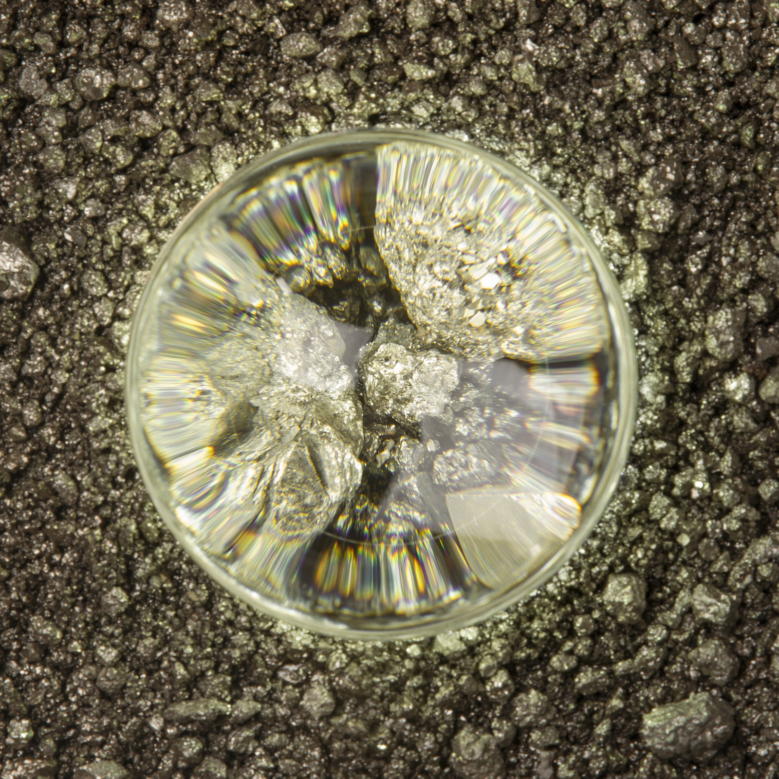 close up of illuminated glass lens in center, magnifying gold color pyrite pieces in warm light