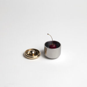 brass ring lid next to steel rounded cup with cherry inside.