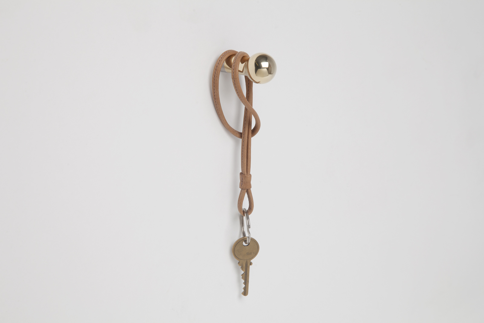 brass wall hook with sphere end and rod body attached to wall with leather keychain hanging off