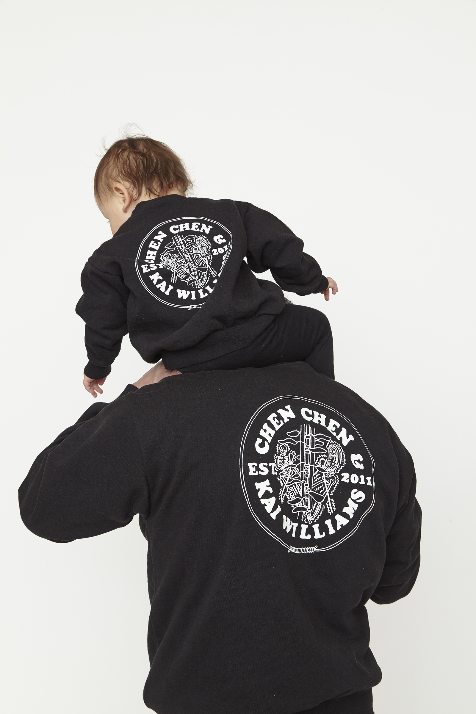 child and adult wearing black sweatshirt with white graphics.