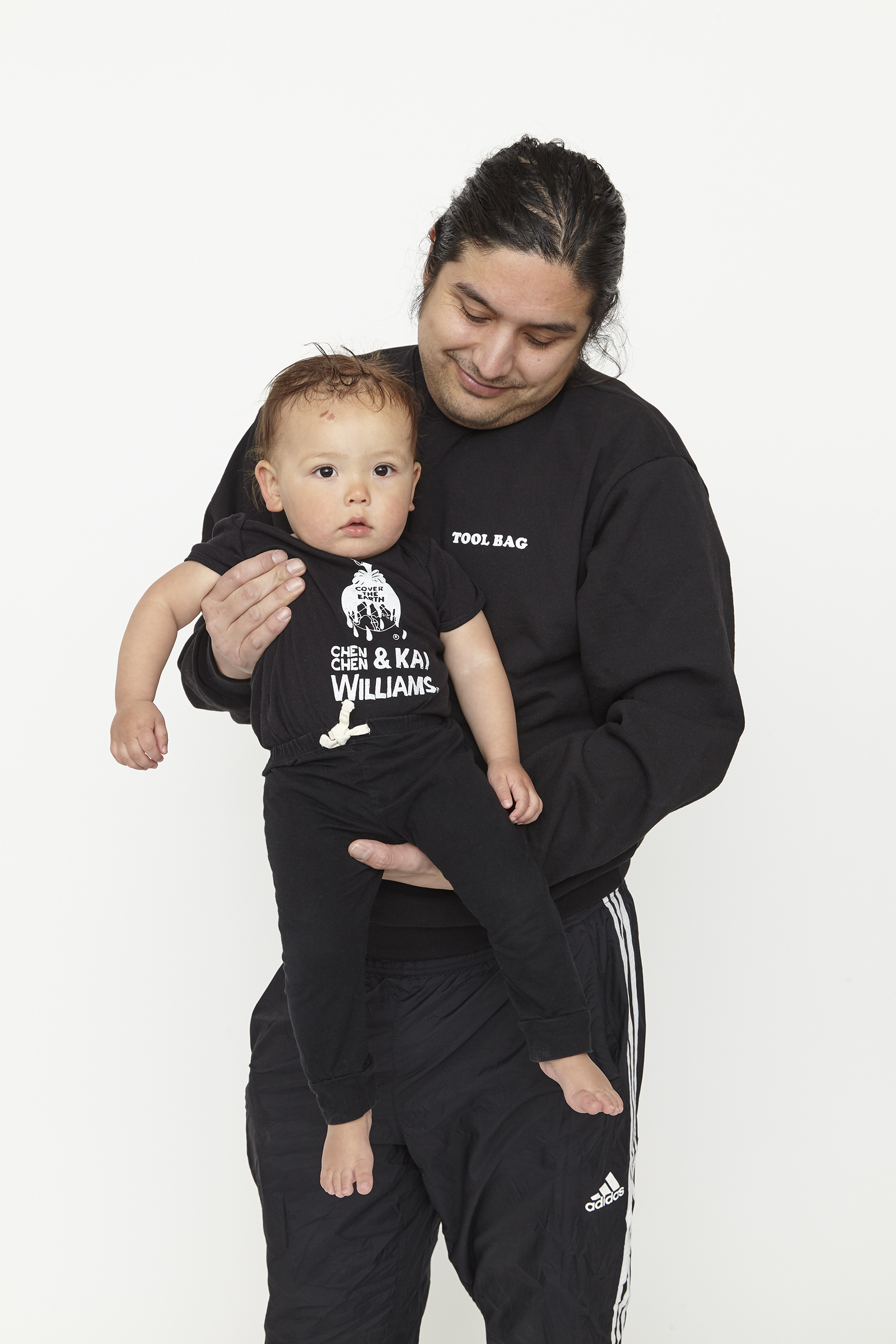 child wearing black onesie with white graphics in front of man with black sweatshirt and white graphics