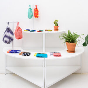 White multi tiered shelving with colorful bags and a potted plant on it.