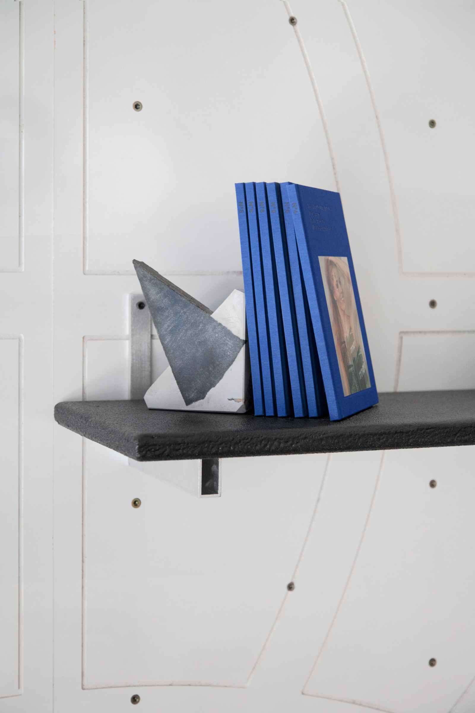 white wall with black shelving and blue books.