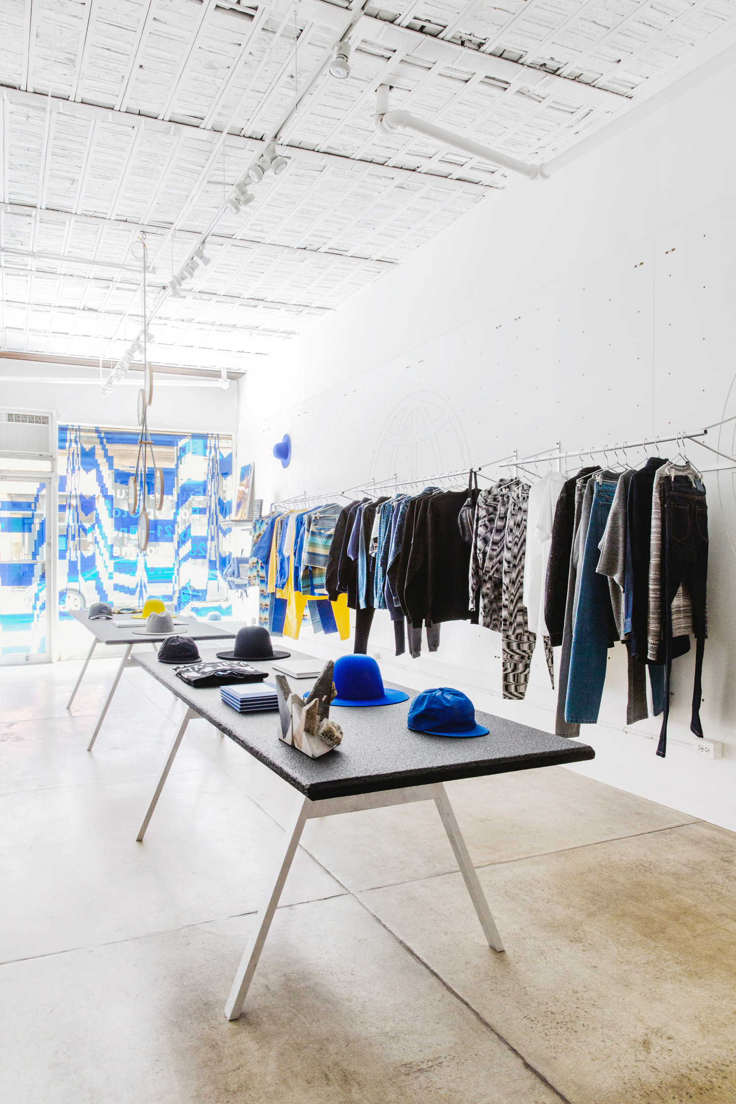 pop up shop with concrete floors and white interior, rack of clothing and table with goods.