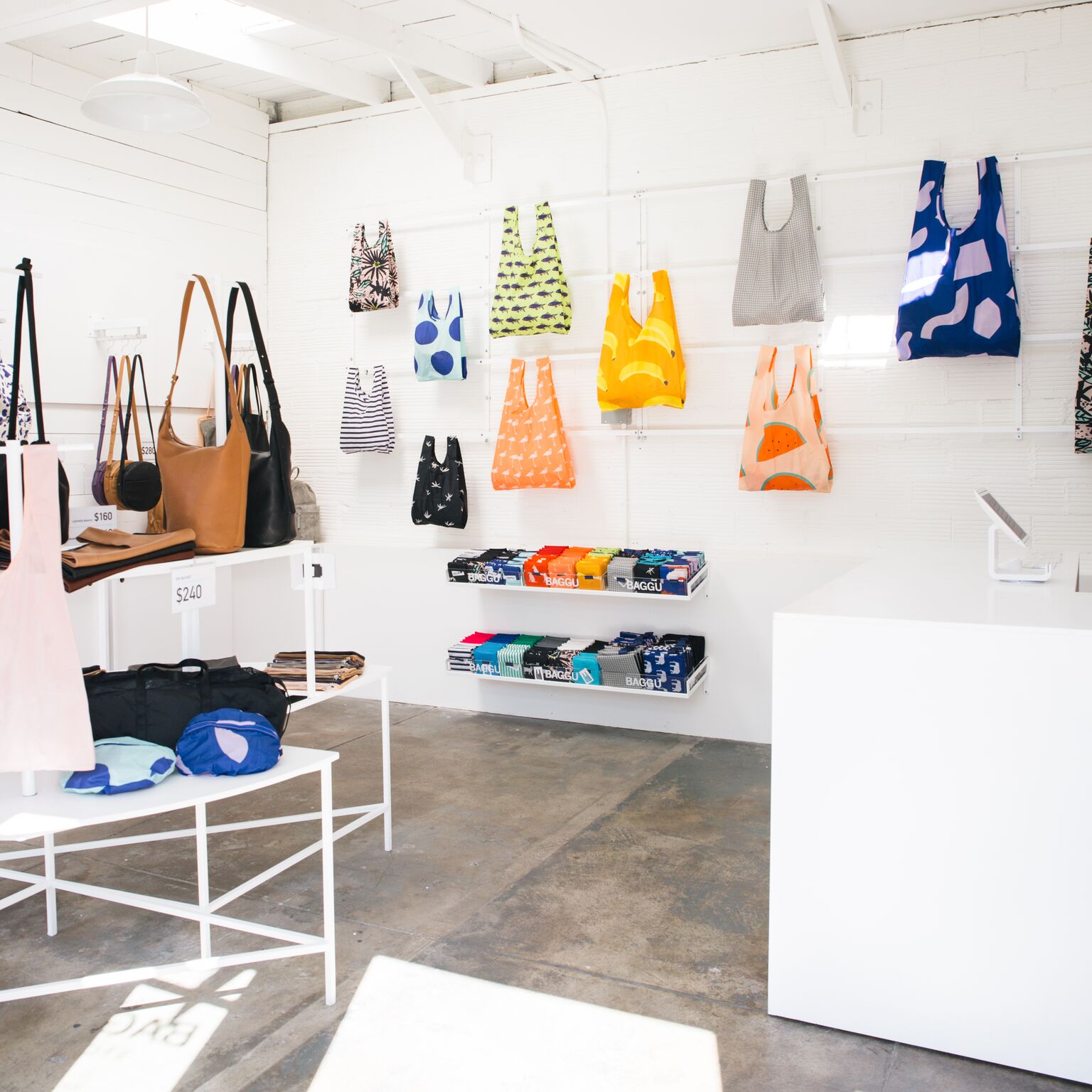 inside of BAGGU store. concrete floors and white interior with colorful bags hanging on walls.