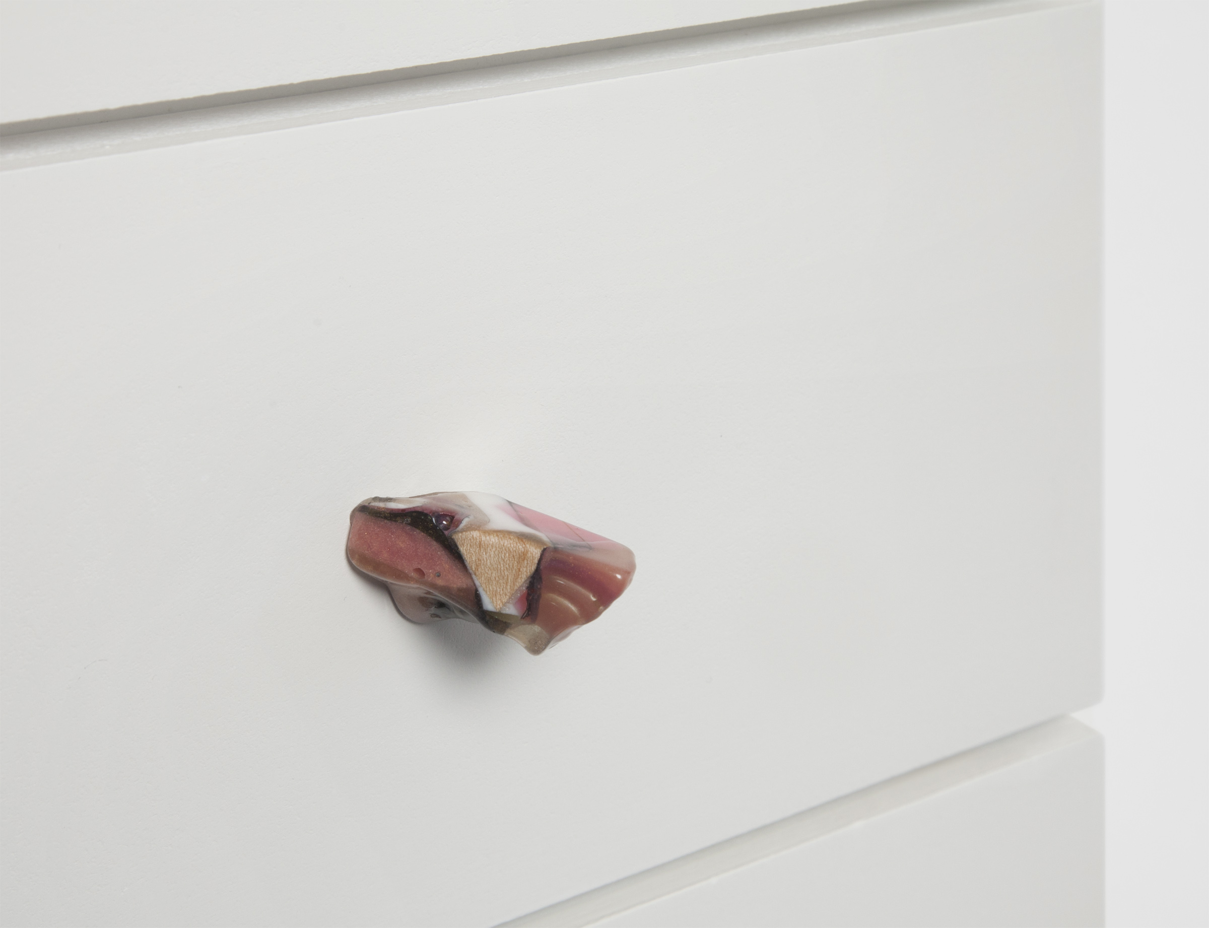 A colorful resin drawer pull on a white drawer front