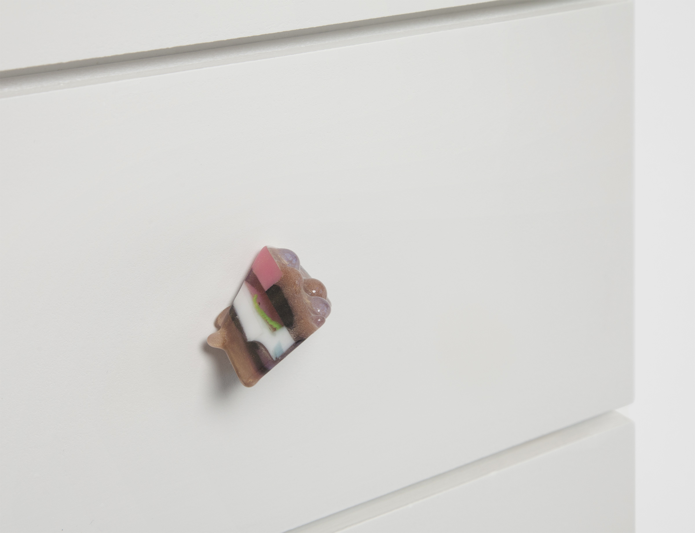 A colorful resin drawer pull on a white drawer front