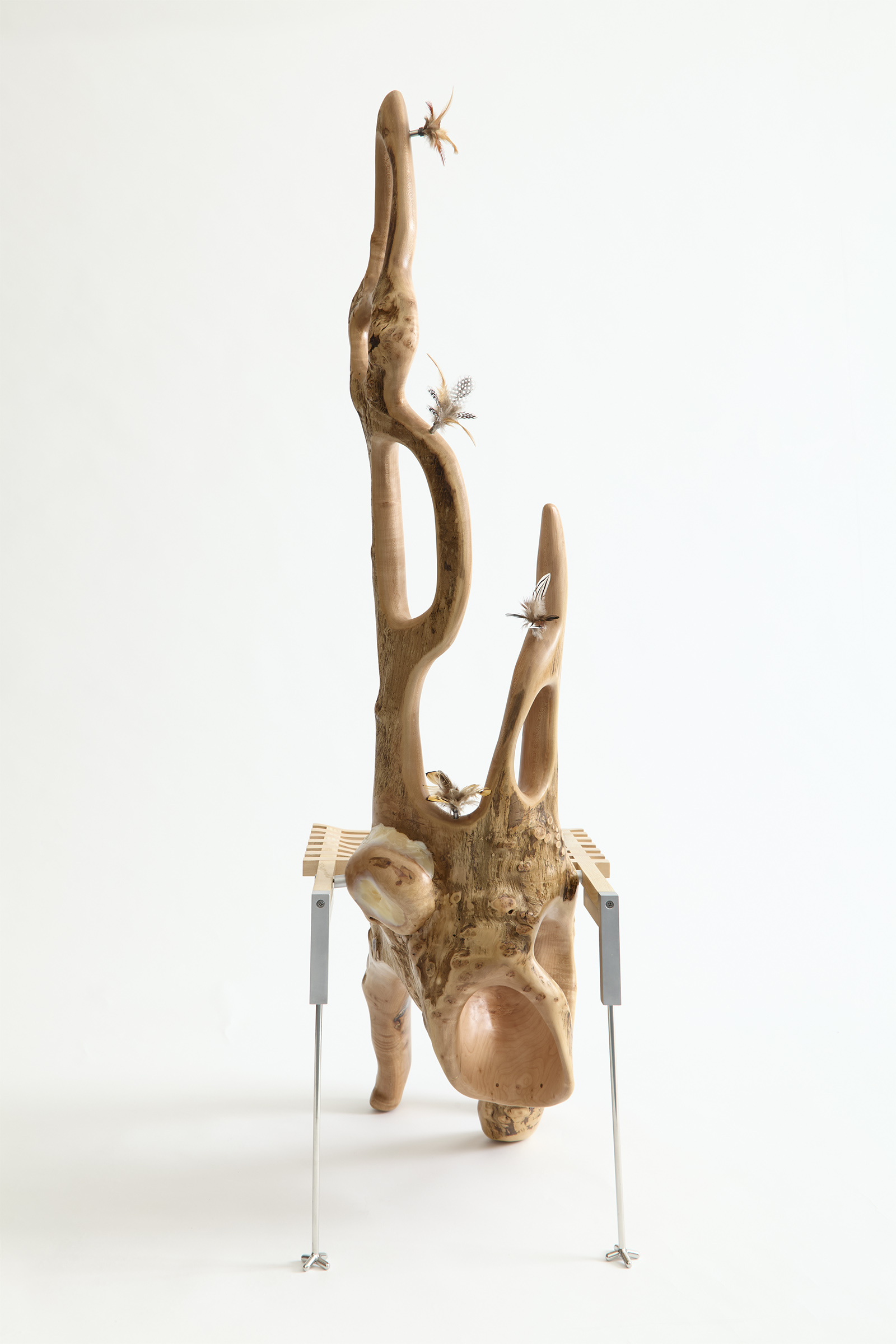 chair carved from a maple log with a grid shaped seat and metal back legs decorated with feathers