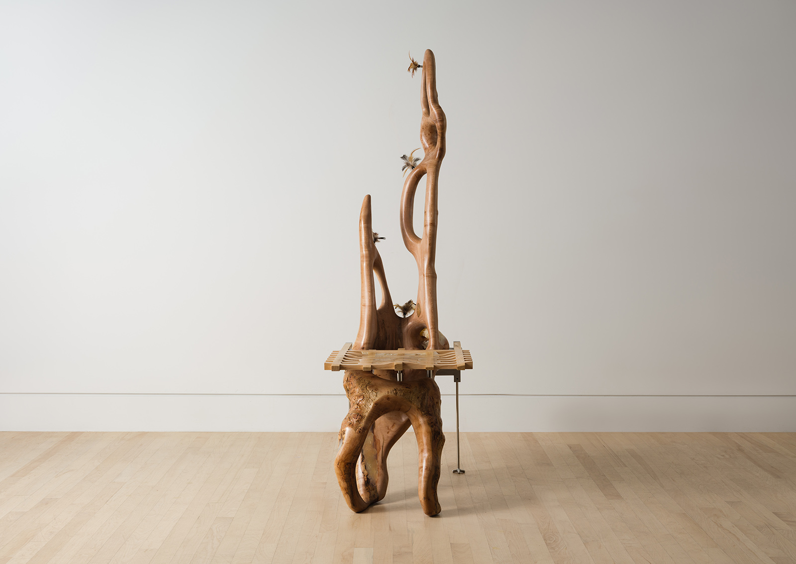 chair carved from a maple log with a grid shaped seat and metal back legs decorated with feathers