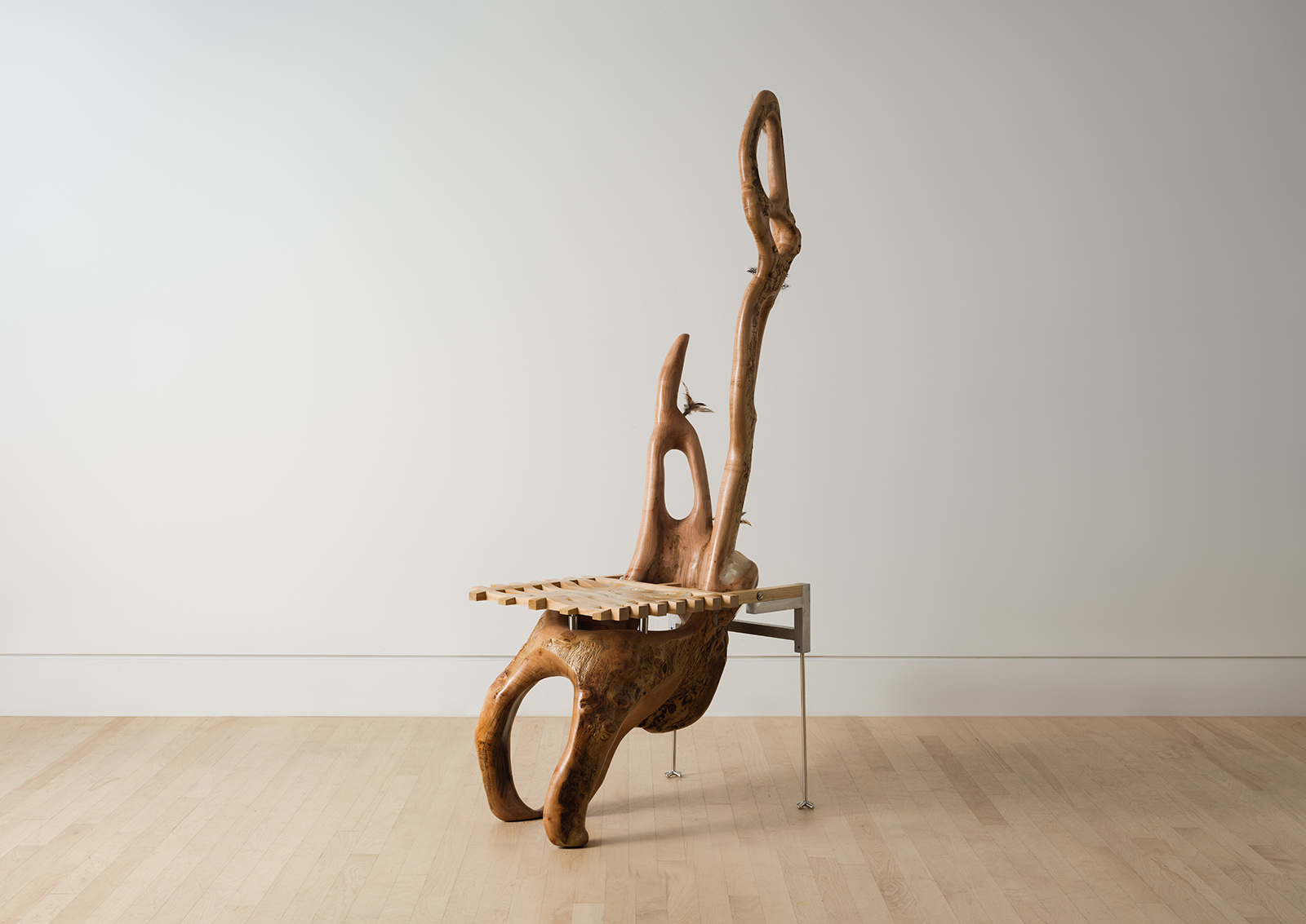 chair carved from a maple log with a grid shaped seat and metal back legs decorated with feathers