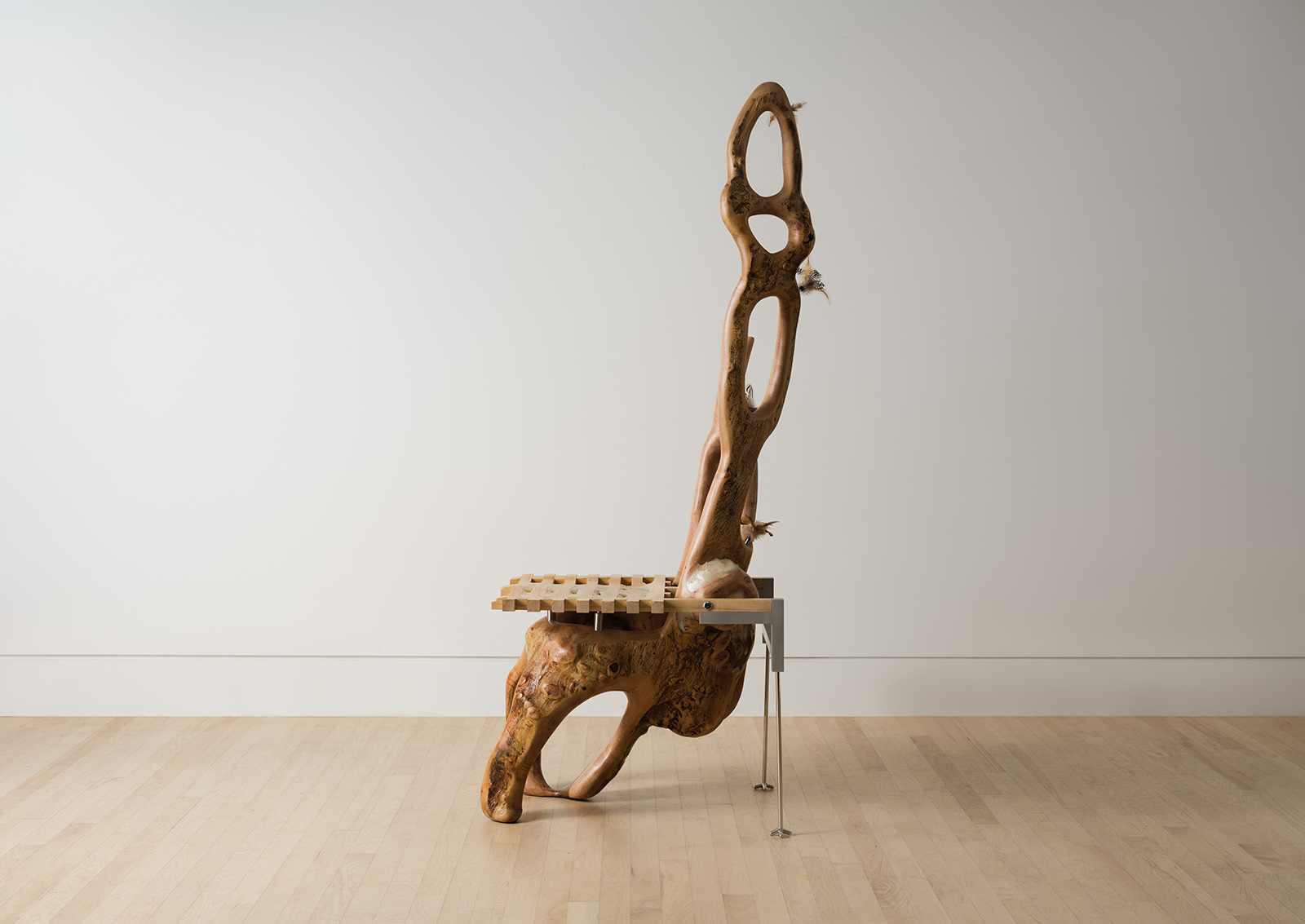 chair carved from a maple log with a grid shaped seat and metal back legs decorated with feathers