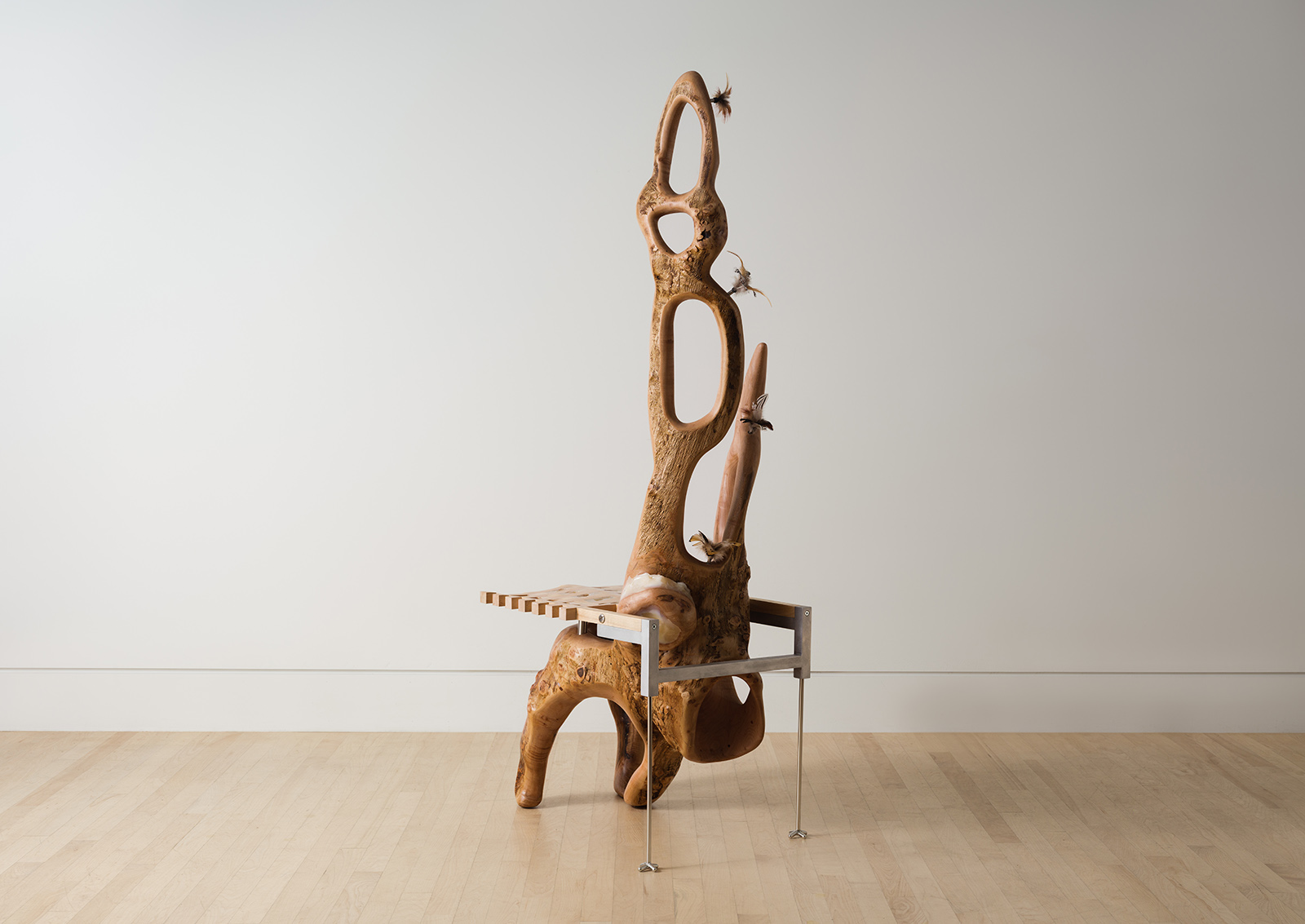 chair carved from a maple log with a grid shaped seat and metal back legs decorated with feathers