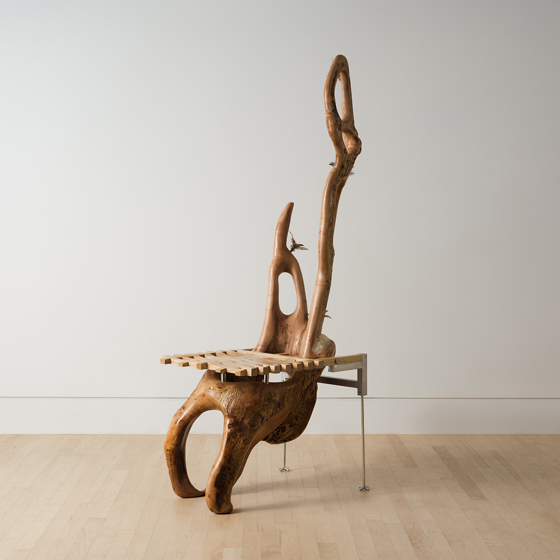 chair carved from a maple log with a grid shaped seat and metal back legs decorated with feathers