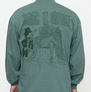detail of back of longsleeve graphic shirt with a drawing of a log as a woman and a woodpecker. Text says "Basic Instinct"