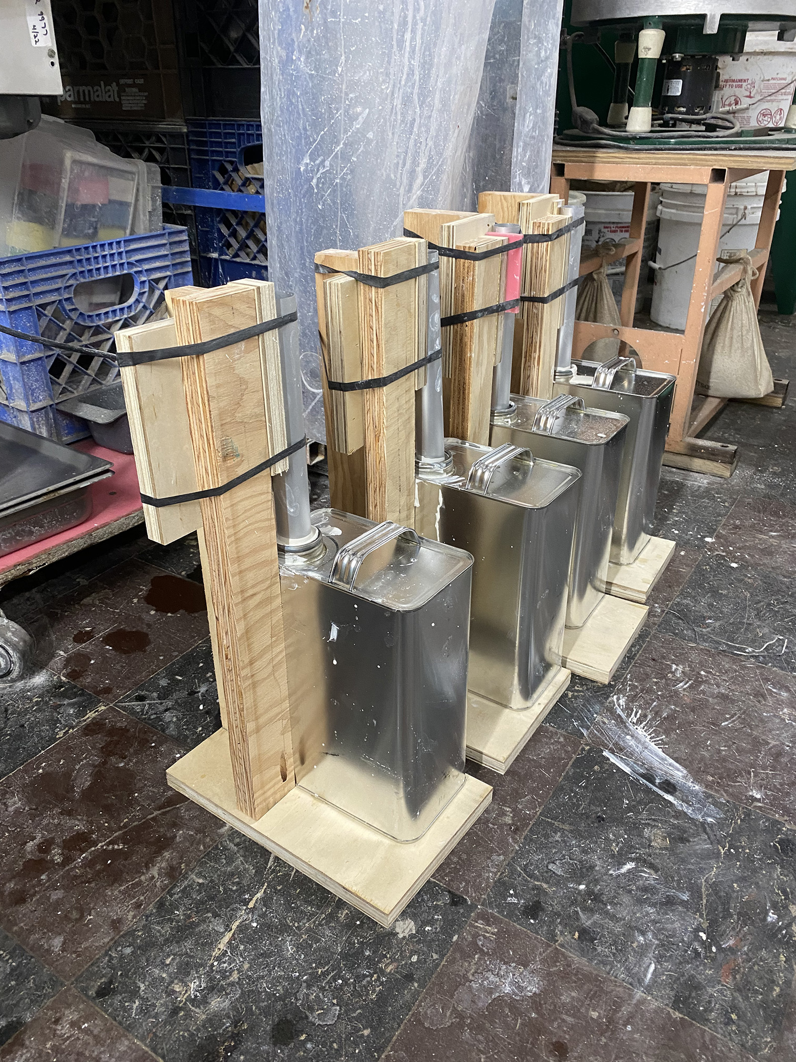 four metal jugs with a round bar sticking out of the mouth filled with plaster in a wood jig