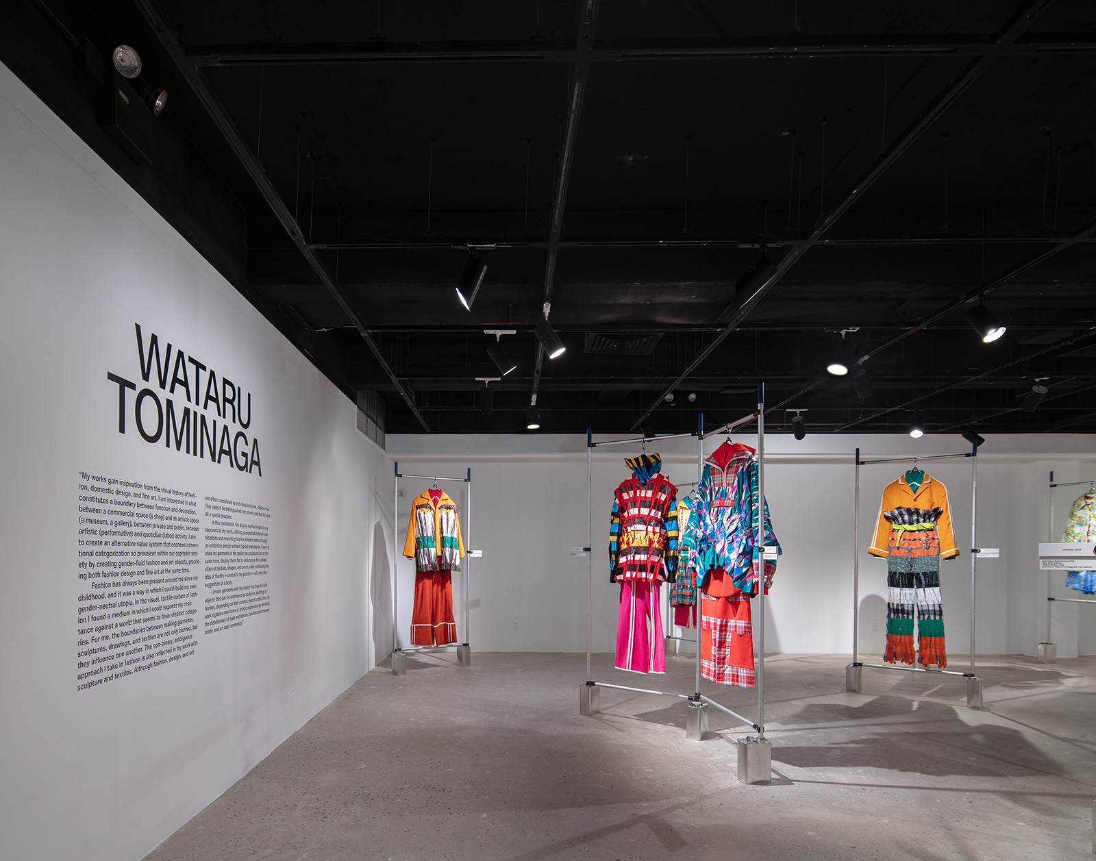 museum exhibition with 4 clothing sets hanging on a metal bar system