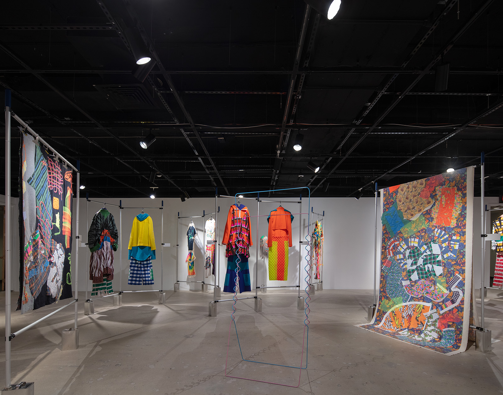 museum exhibition with clothing sets and fabrics hanging on a metal bar system