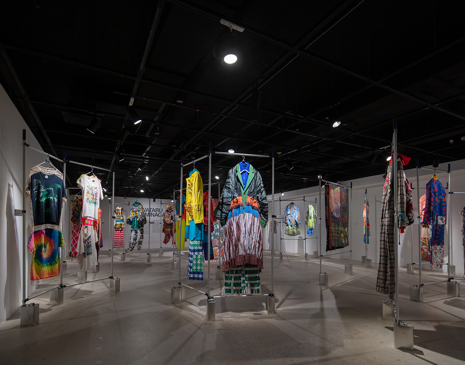 museum exhibition with clothing sets and fabrics hanging on a metal bar system