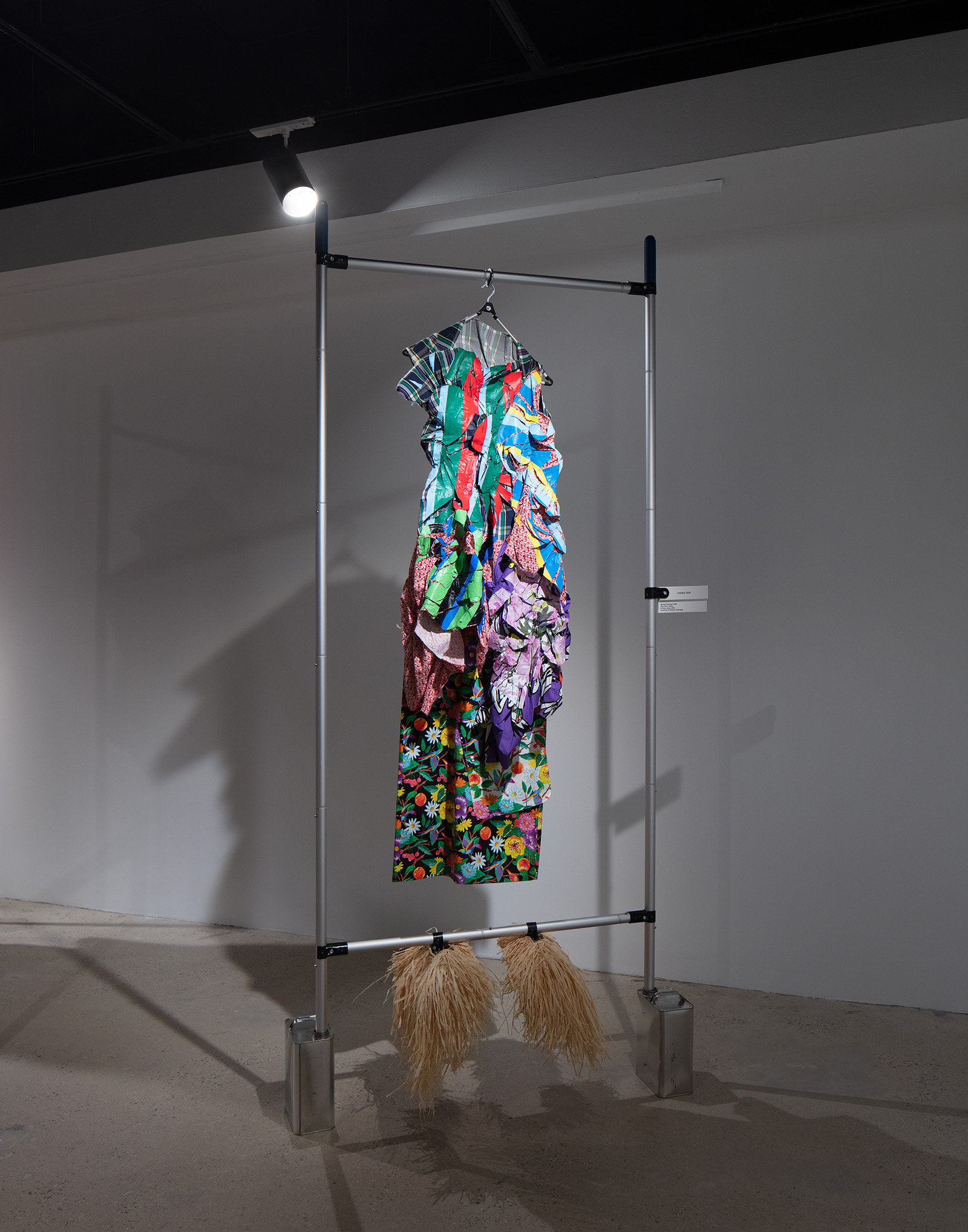 a set of colorful clothing with straw shoes hanging on a metal bar armature